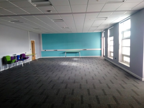 This is a large, carpeted room with windows down one side.