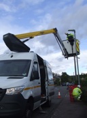 A white van with a cherry picker built into it. There are workers in high visibility clothing replacing a streetlight