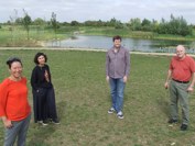 Four people standing at the edge of a lake in Northstowe, surrounded by trees and plants.