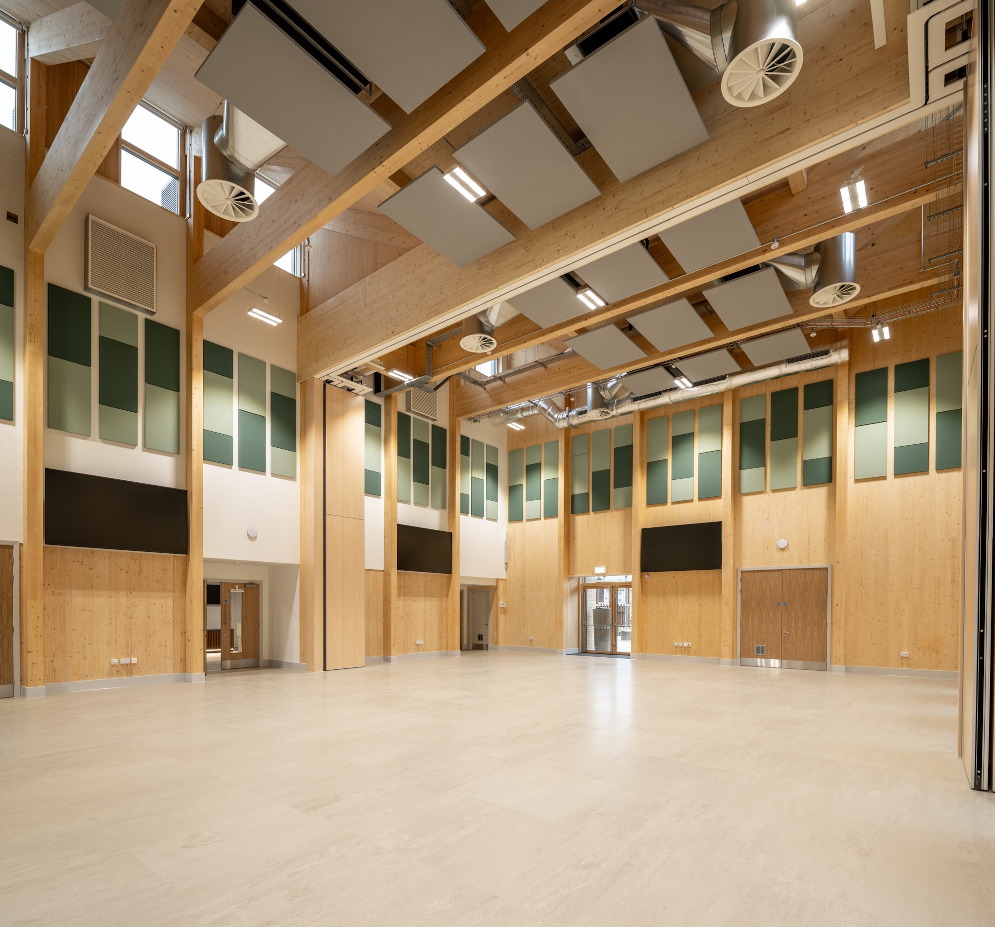 Large multi-use hall inside Northstowe Unity Centre with exposed timber beams, acoustic panels and high ceiling.