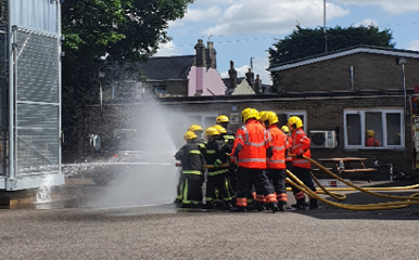 Fire service personnel with group of schoolchildren demonstrating use of a fire hose