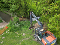 An orange digger parked at the edge of the River Mel. The digger is being used to place gravel along the riverbed. To the side, a Council operative is helping to smooth the newly-deposited gravel out.