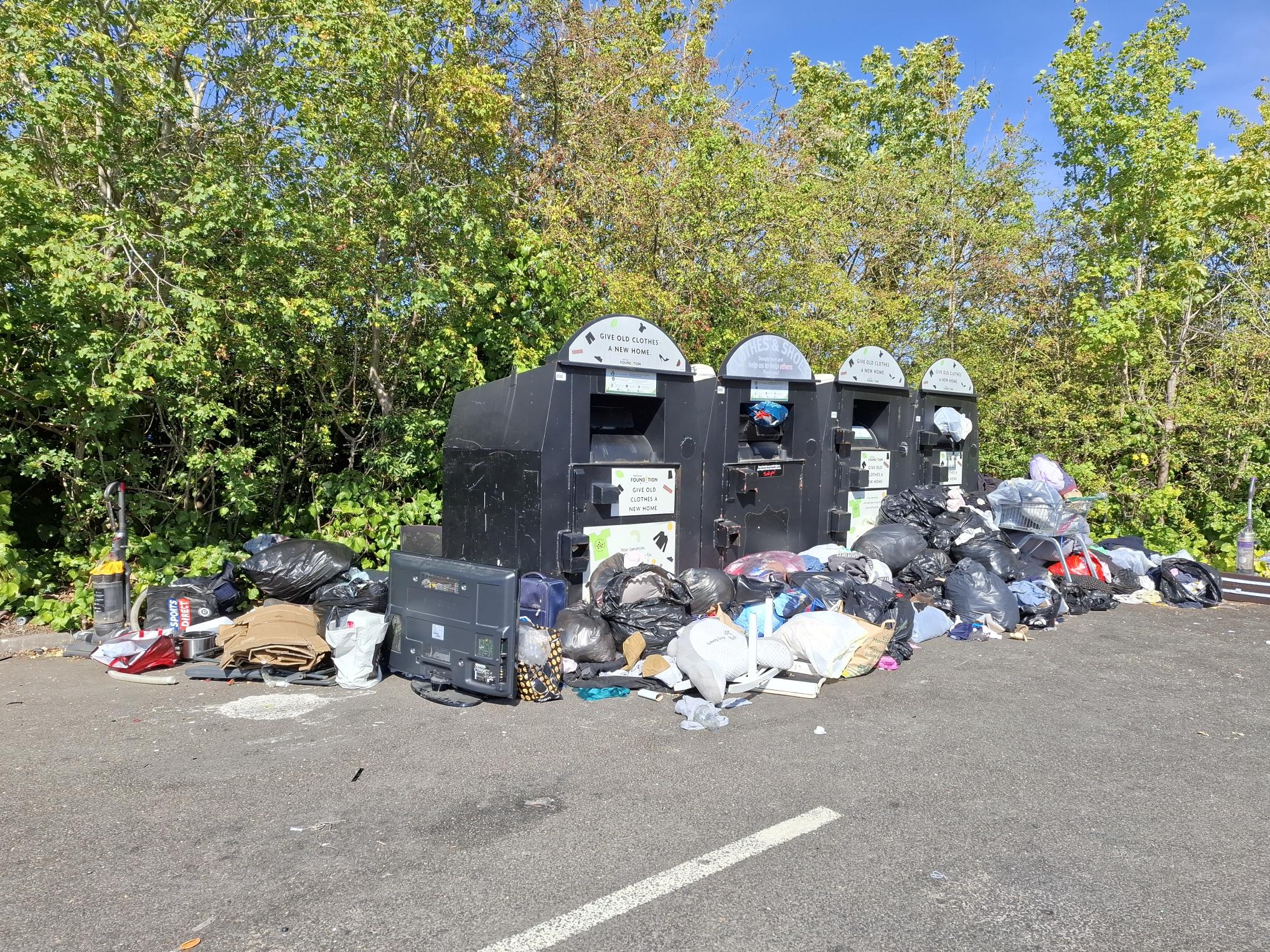 Large amounts of waste, including black bags, cardboard, household items and a television, left beside clothing recycling banks at a recycling area in Cambourne.