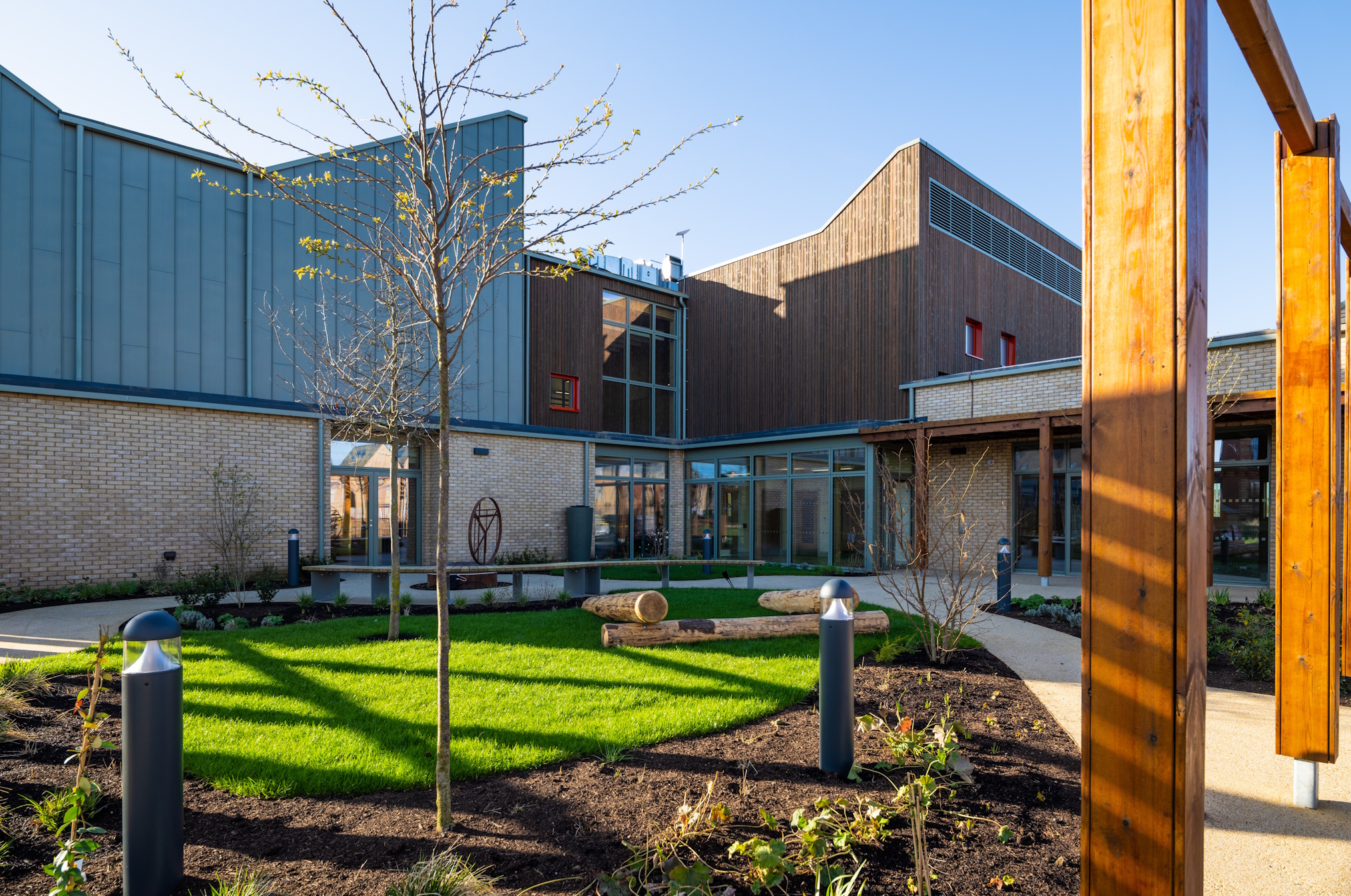 Landscaped courtyard at Northstowe Unity Centre with young trees, seating areas and timber-clad buildings surrounding a central green space.
