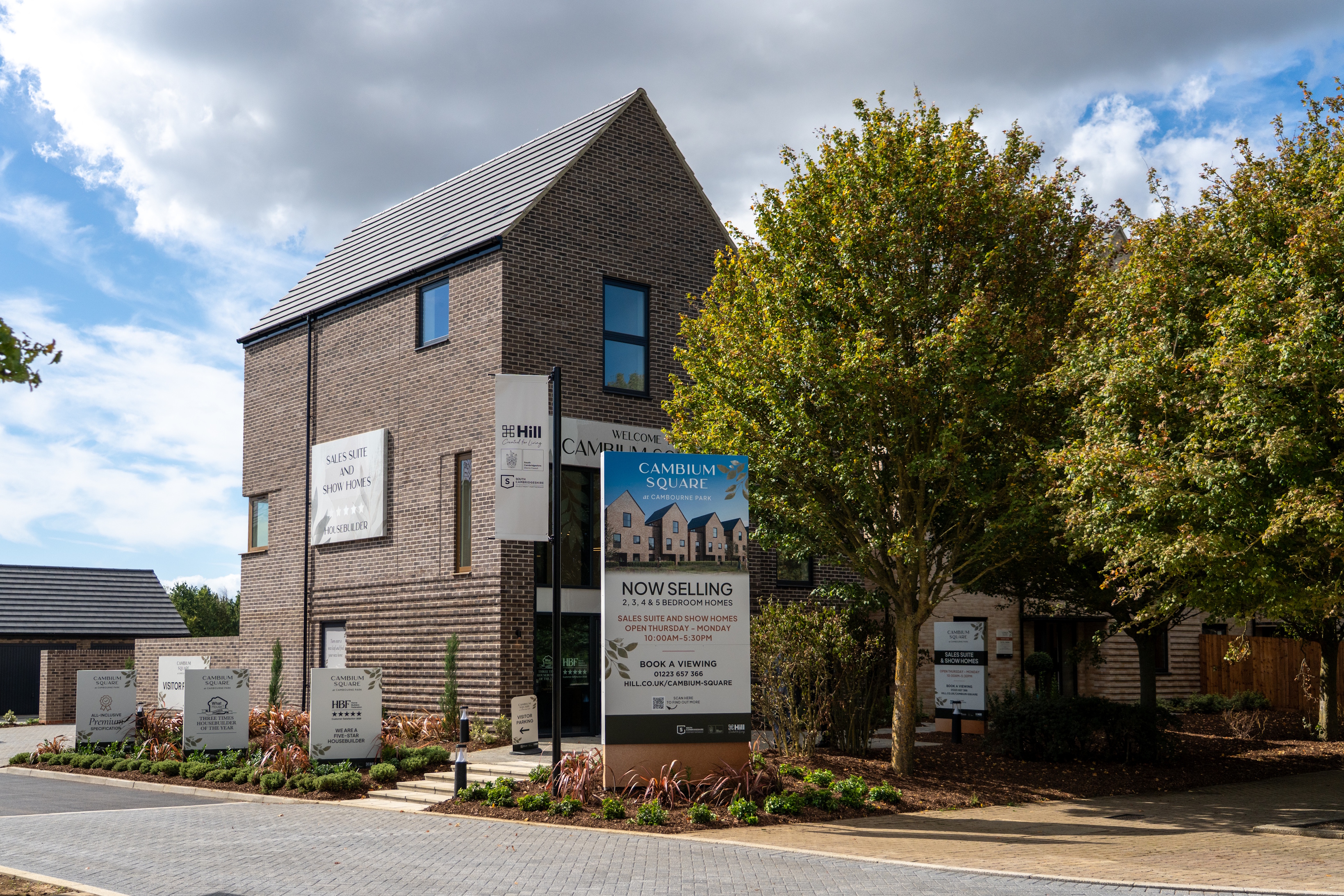 Exterior view of the Cambium Square sales suite and show homes at Cambourne Park, featuring landscaped planting, promotional signage and newly built homes.
